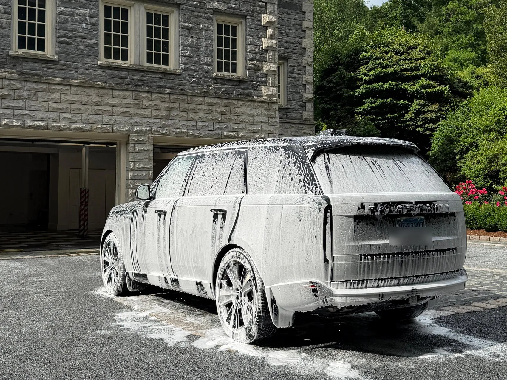 A Range Rover under a full coat of snow foam on the gravel drive of a large stone house.