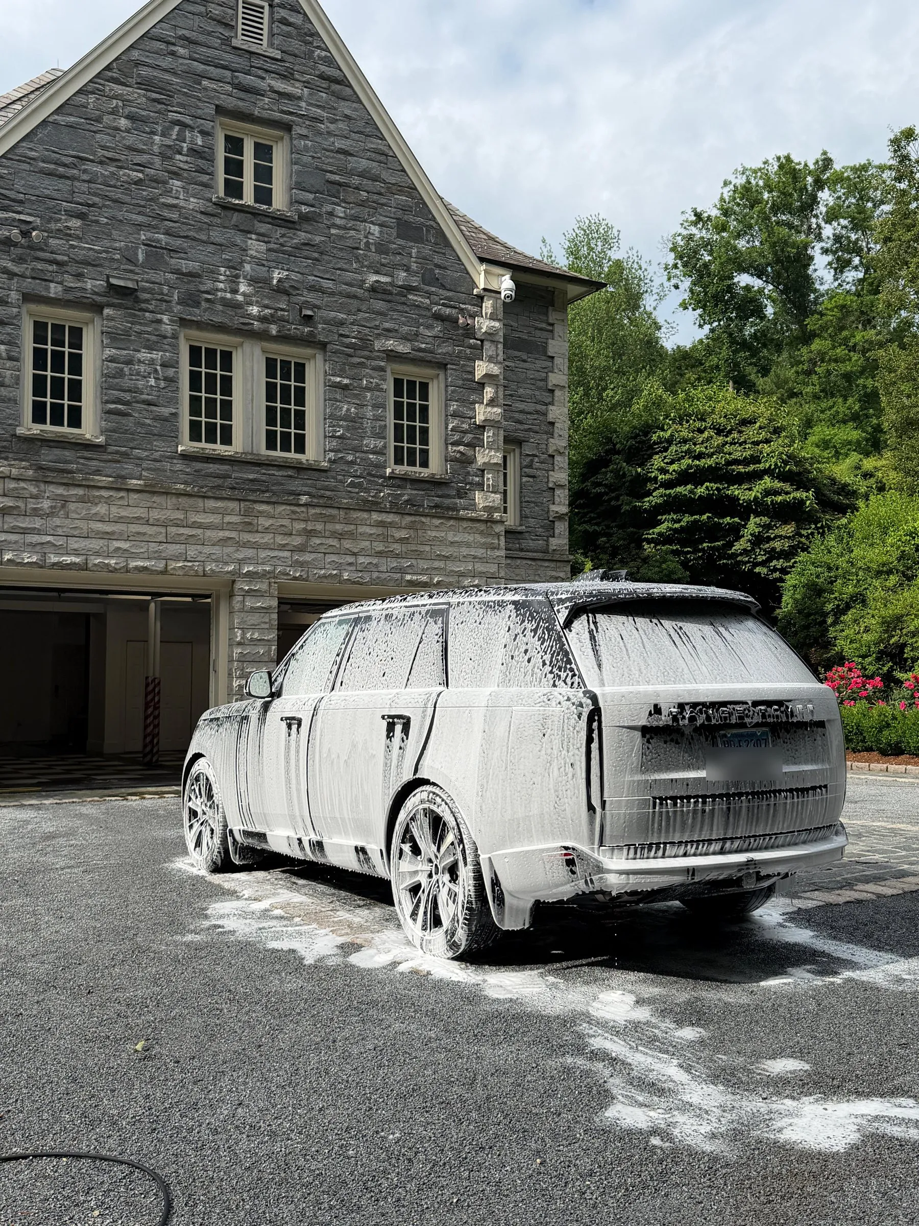 A Range Rover covered in snow foam on the gravel drive of a large stone house.